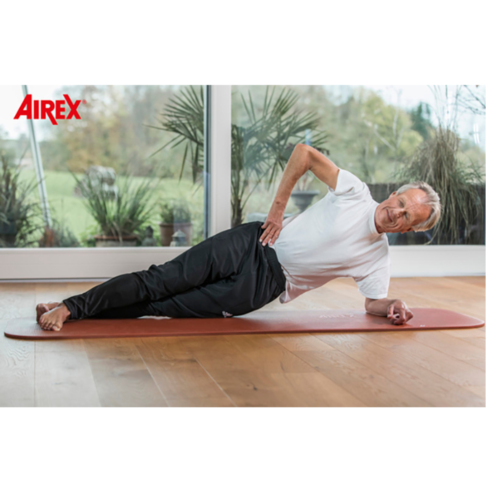 Man exercising on a red Airex mat in a room with large windows and greenery outside.